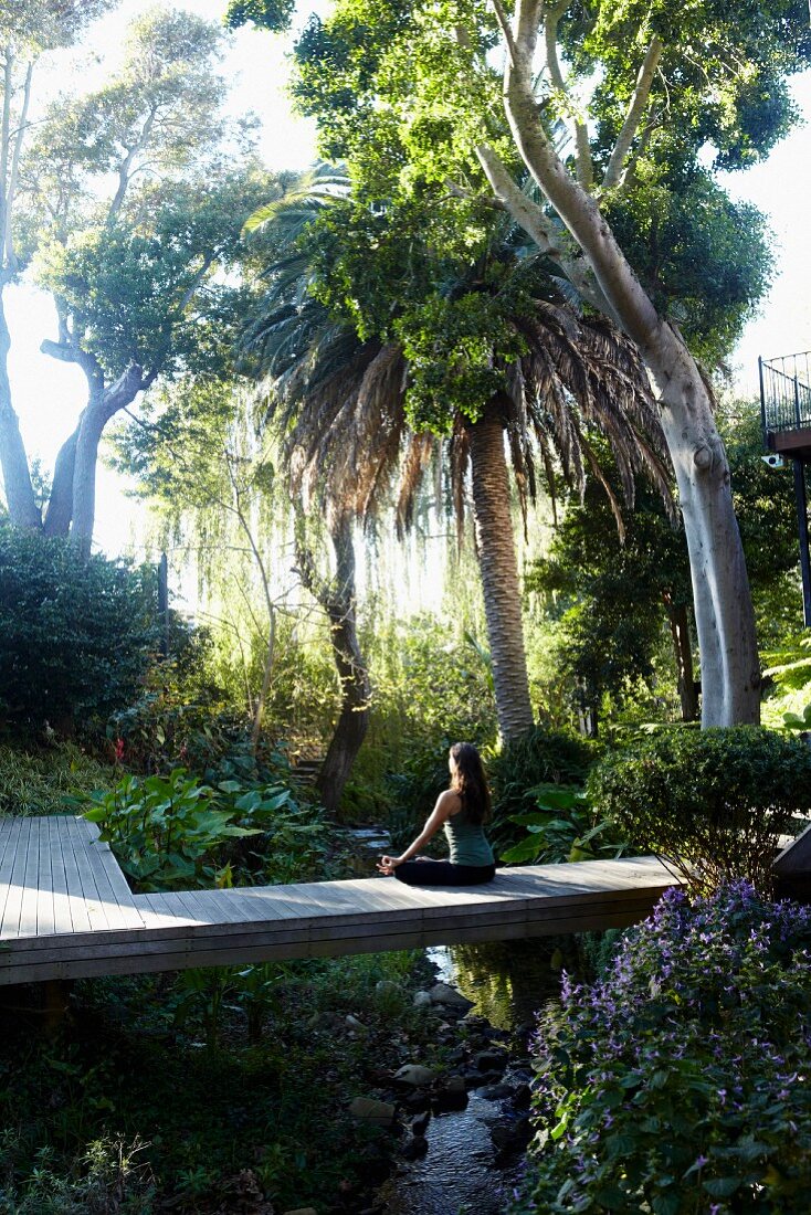 Woman meditating on wooden bridge in tropical garden