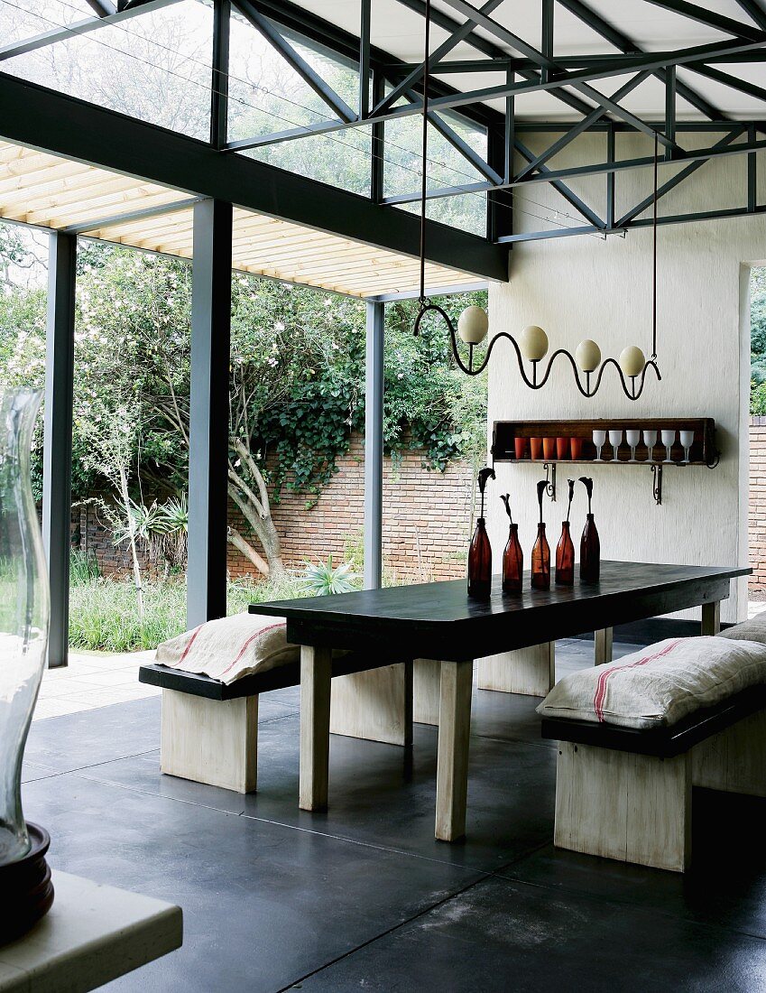 Rustikaler Esstisch mit passenden Bänken unter angefertigter Hängeleuchte in hallenartigem Wohnraum mit geöffneten Terrassentüren