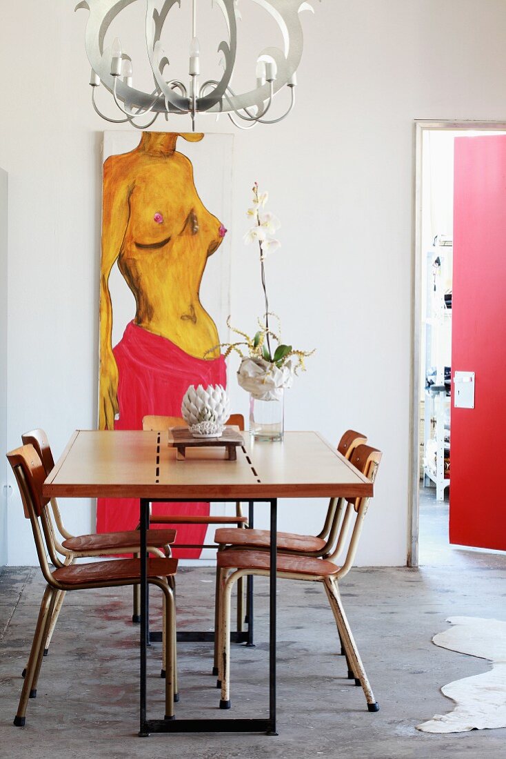 Dining table with metal frame and retro chairs below postmodern pendant lamp; painting on wall in background