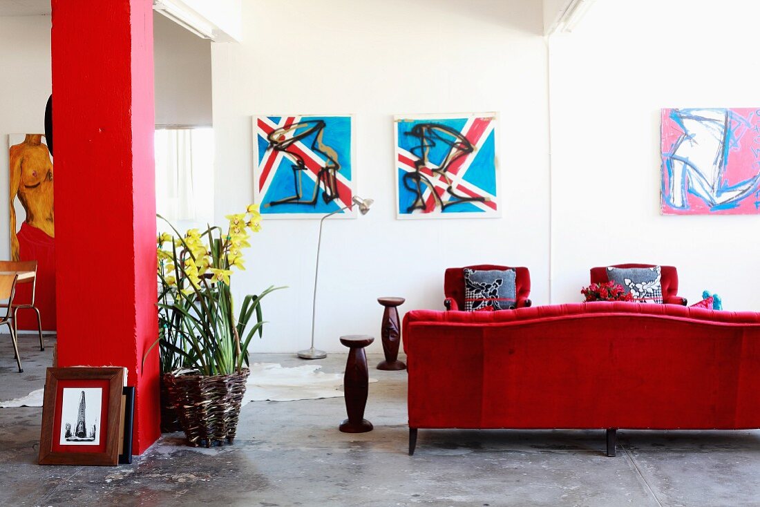 Loftariger Wohnraum mit rotem Sofa und Sesseln auf grauem Estrichboden neben roter Stütze