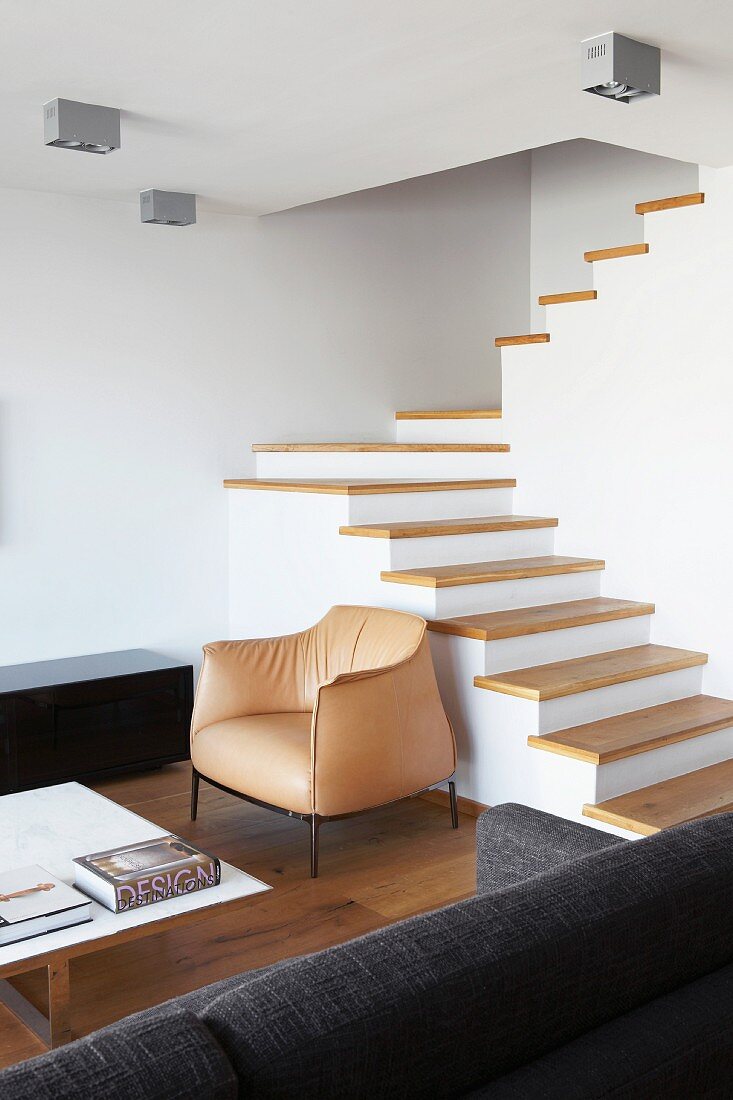 Staircase with wooden treads and no handrail in minimalist, open-plan living area of architect-designed house