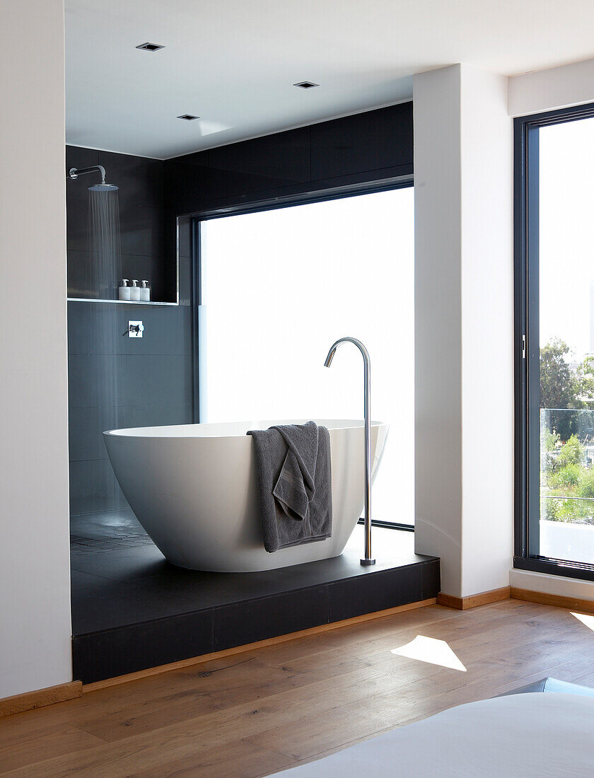 Purist ensuite bathroom with free-standing, white, designer bathtub and shower area on black platform