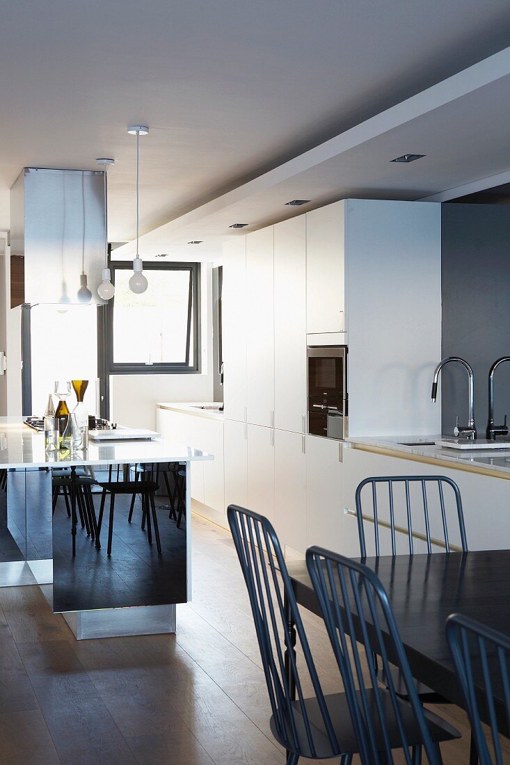 weiße Designer Einbauküche mit verspiegeltem Küchenblock und schwarzem Esstisch mit filigranen Stühlen