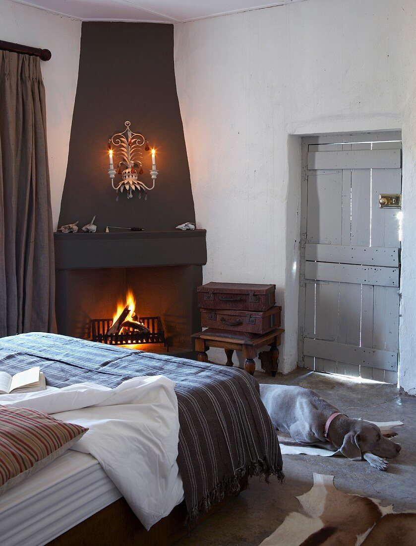 Bedroom with cosy open fire in corner fireplace - dog on floor at foot of bed