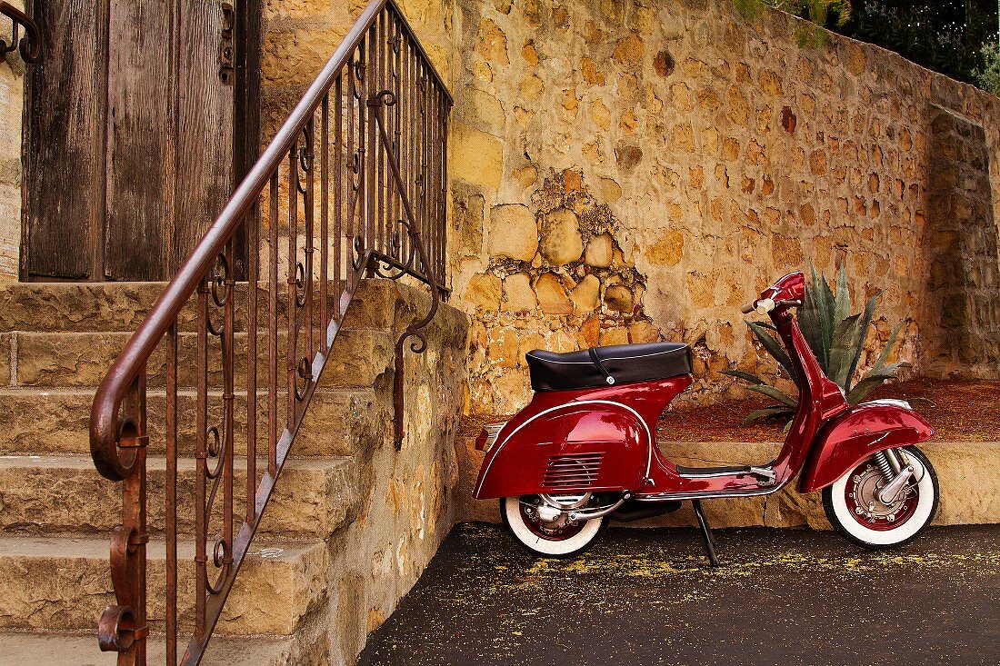 Roter Vespa Motorroller, an einer Steinmauer geparkt