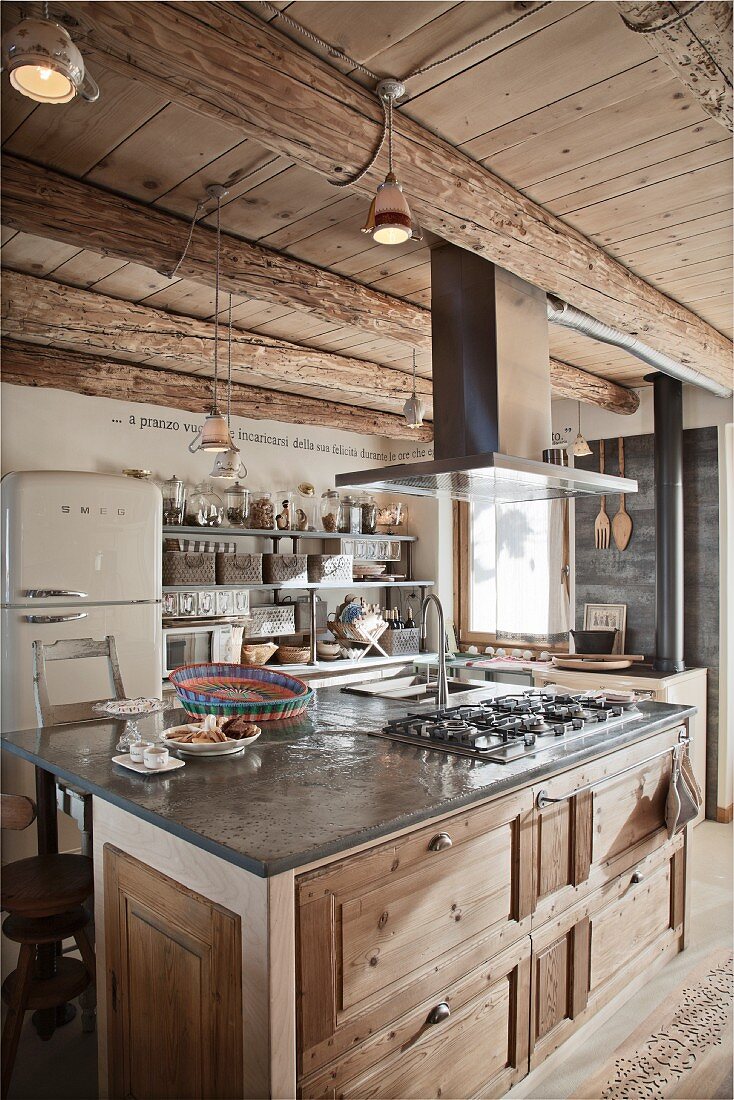 Rustic island counter with stainless steel extractor hood in open-plan interior of wooden chalet