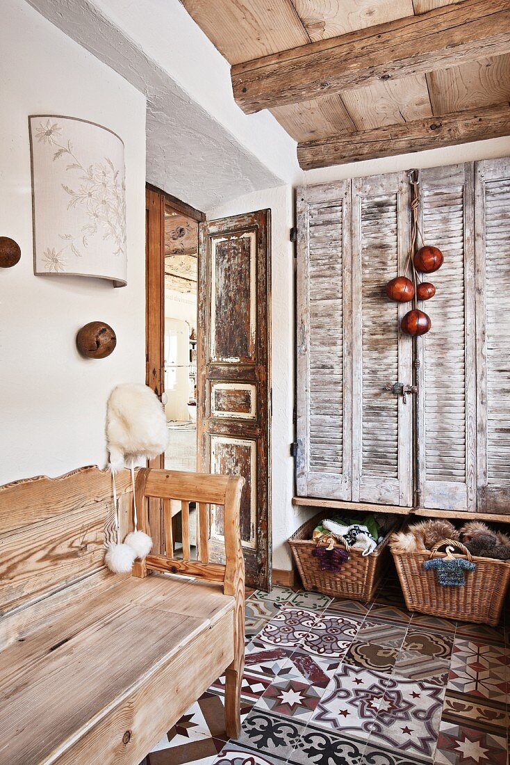 Flurbereich mit rustikaler Holzbank auf gemustertem Fliesenboden und Innenfensterläden im Vintagestil