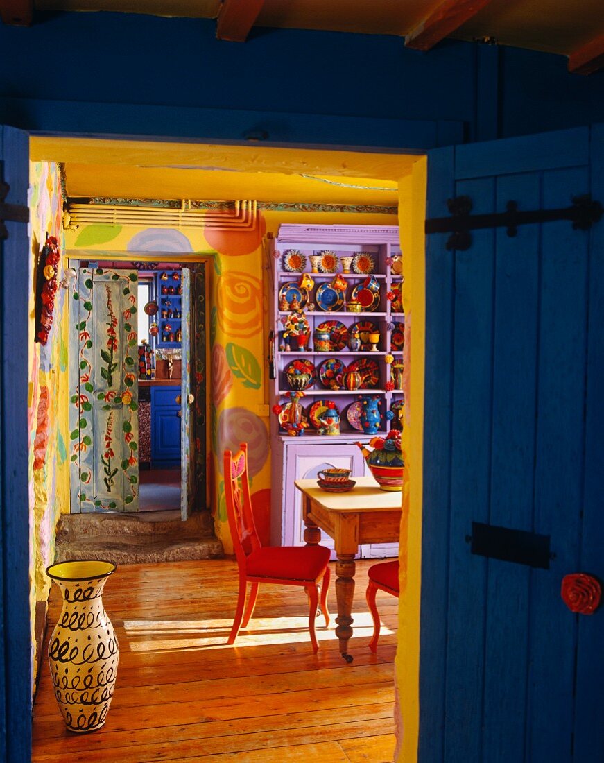 Blick durch geöffnete Holztür in bunt bemaltes Esszimmer mit bunten Tellern in Wandschrank