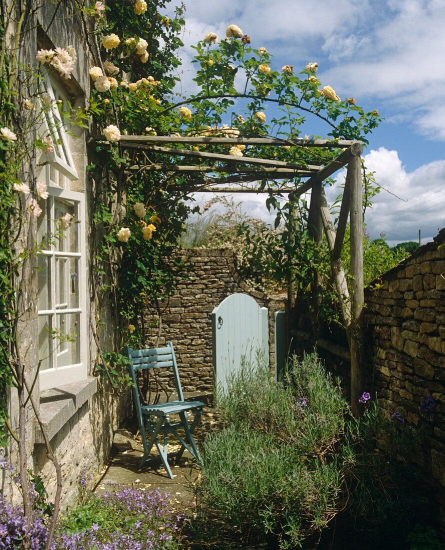 Klappstuhl auf kleiner Terrasse unter rosenberankter Pergola eines Landhauses