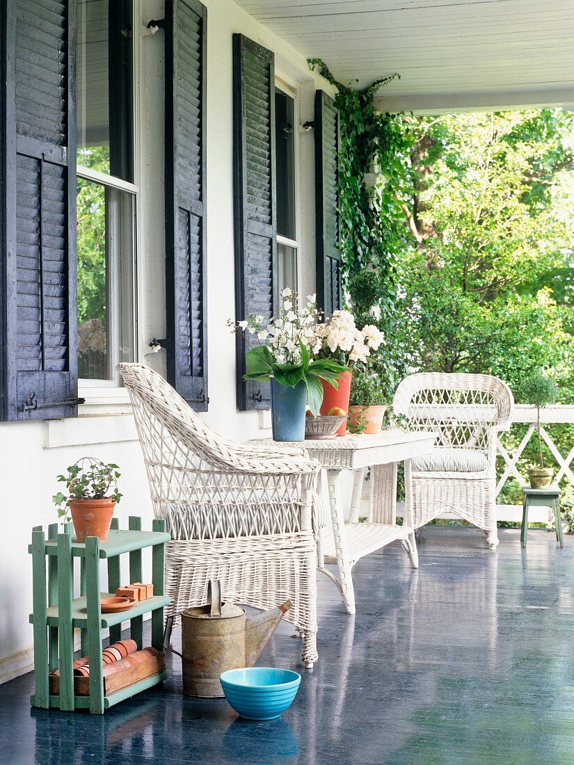 weiße Korbmöbel auf der Veranda vor Hauswand mit blauen Fensterläden