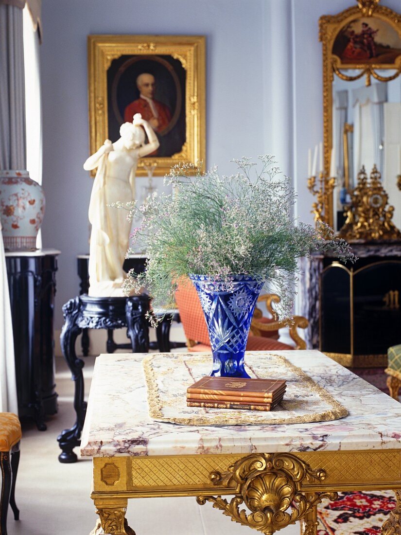 Wohnzimmer mit blauer Kristallvase auf Tisch mit vergoldeten Schnitzereien und Antiquitäten im Hintergrund