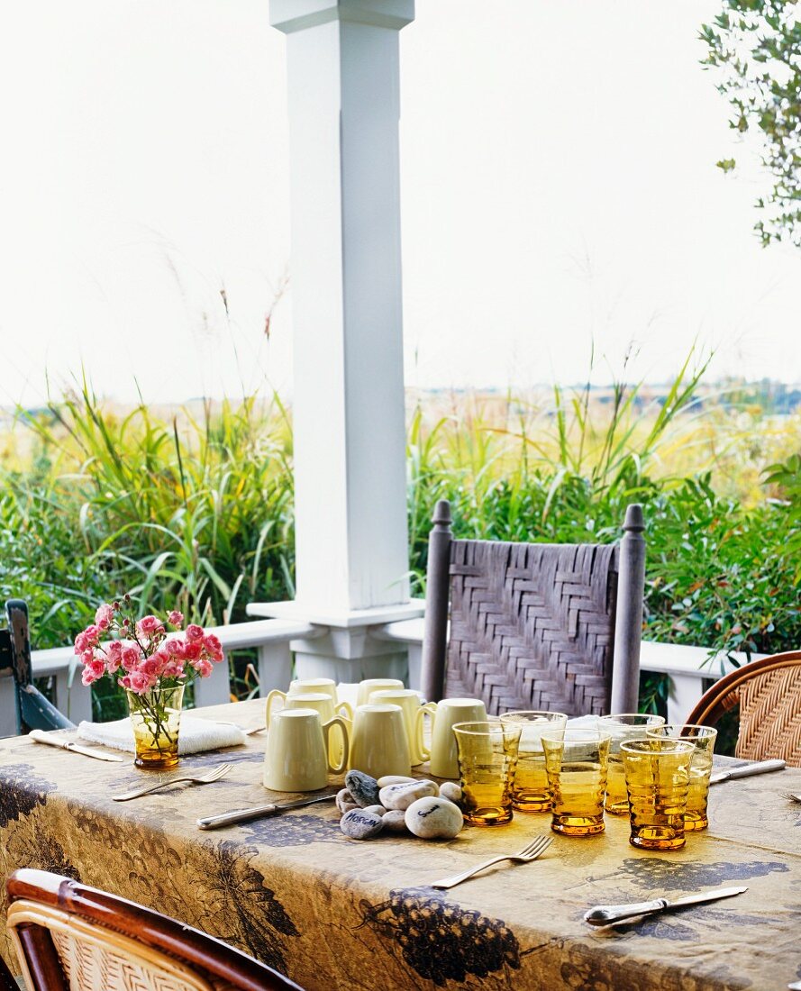 Becher und Gläser auf gedecktem Tisch einer Veranda in sommerlicher Stimmung
