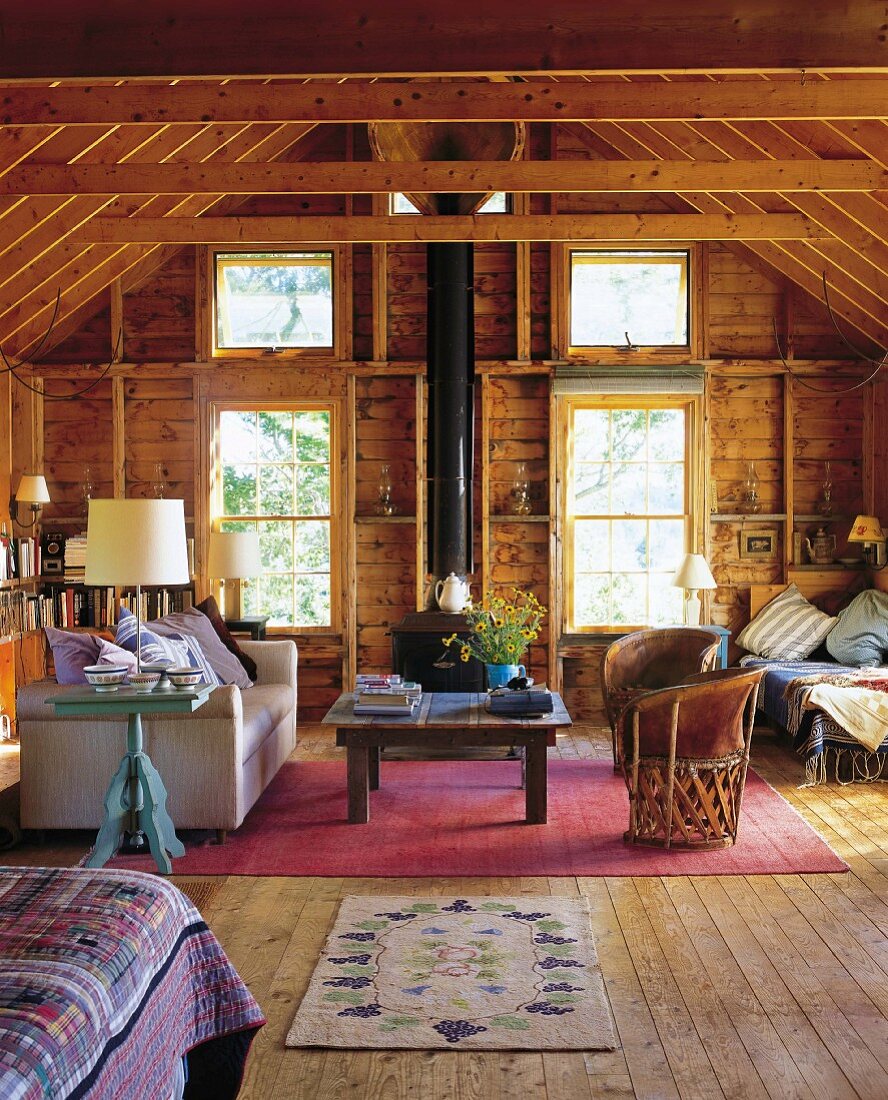 Teilweise sichtbares Bett und Wohnbereich mit modernem Sofa und Vintage Ledersessel in rustikaler Holzhütte in Maine