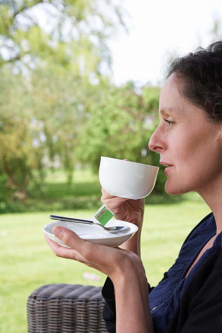 Frau trinkt Tasse Tee auf Terrasse im Garten