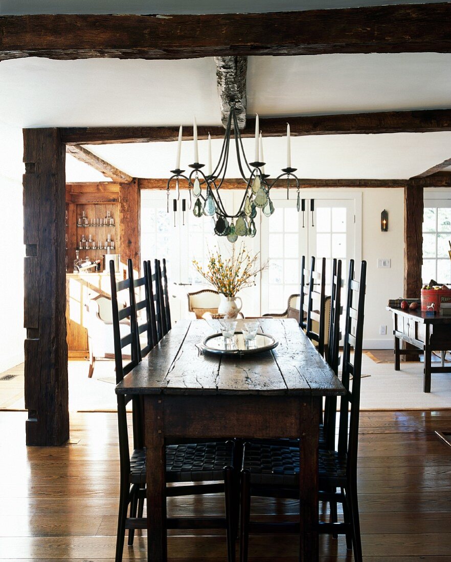 Rittertafel - rustikaler Esstisch mit Stühlen unter schmiedeeisernem Kronleuchter in offenem Wohnraum eines Landhauses