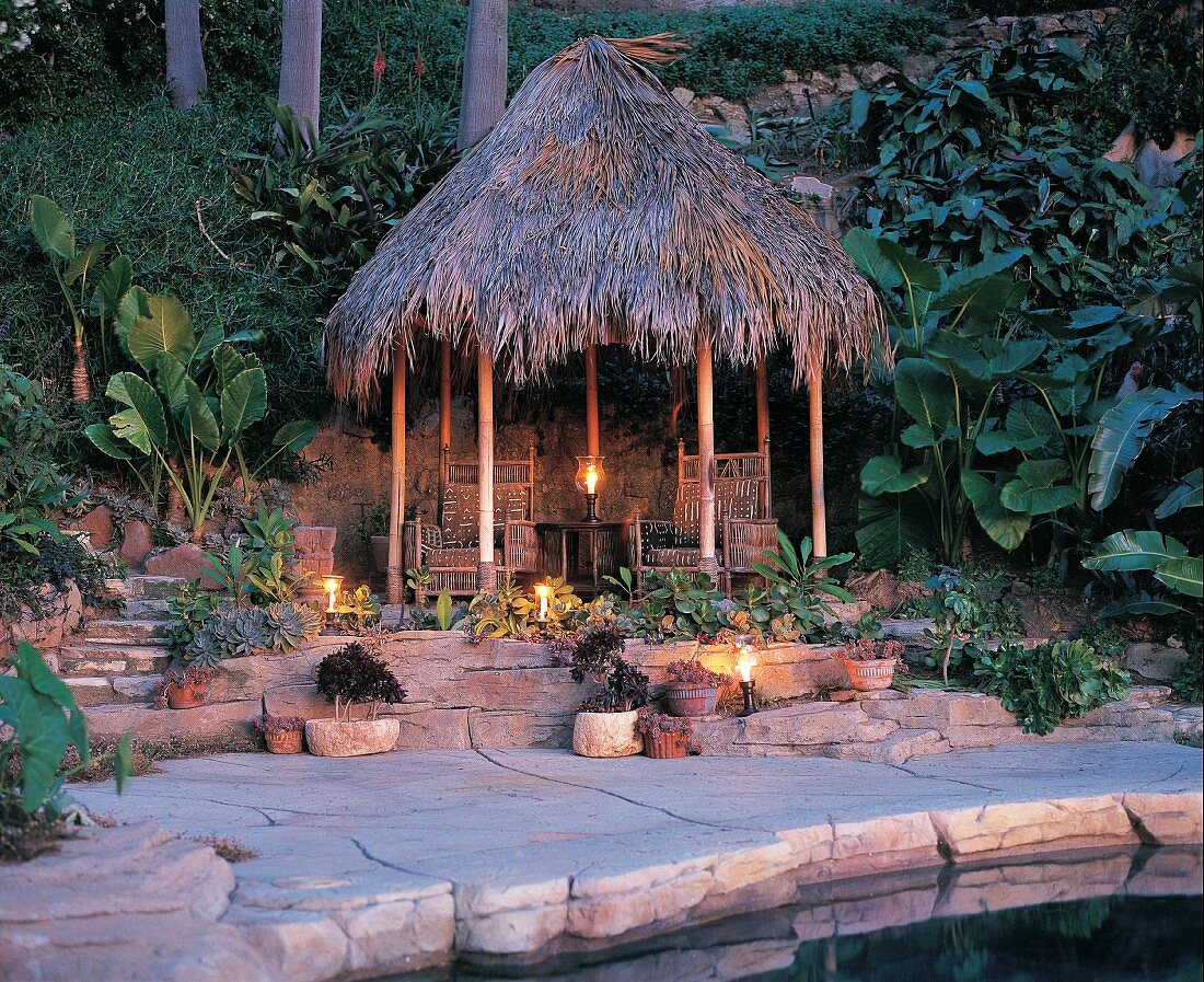 Tiki Hütte am Pool mit Kerzen in tropischen Garten bei Abenddämmerung