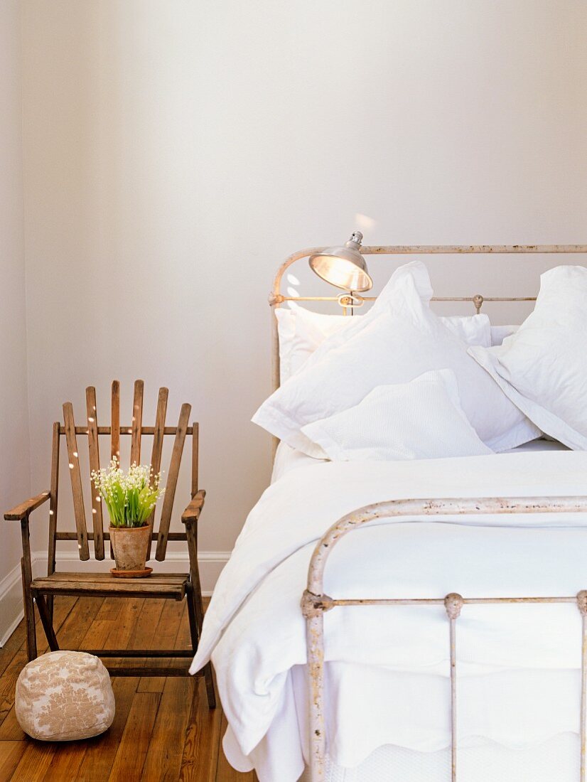 Bett mit Vintage Metallgestell neben schlichtem Holzstuhl mit Blumentopf