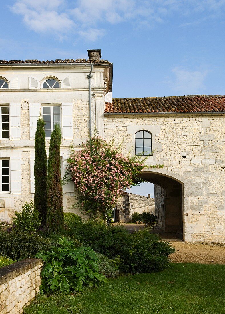 Überbaute Durchfahrt eines alten, französischen Landgutes mit blühenden Rankpflanzen und Zypressen