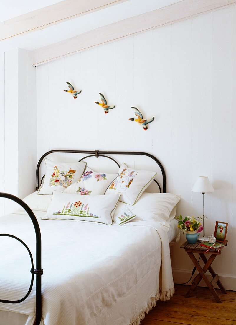 Bunte Vogelfiguren an der Wand über romantischem Metallbett im Landhausstil