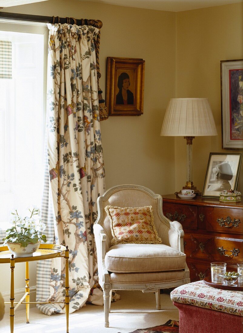 Wohnzimmerecke im altenglischen Landhausstil mit Polstersessel vor floral gemustertem Vorhang und zierlichem Beistelltisch