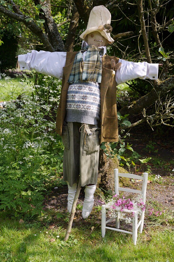 Im englischen Country-Stil gekleidete Vogelscheuche und weisser Kinderstuhl im Garten
