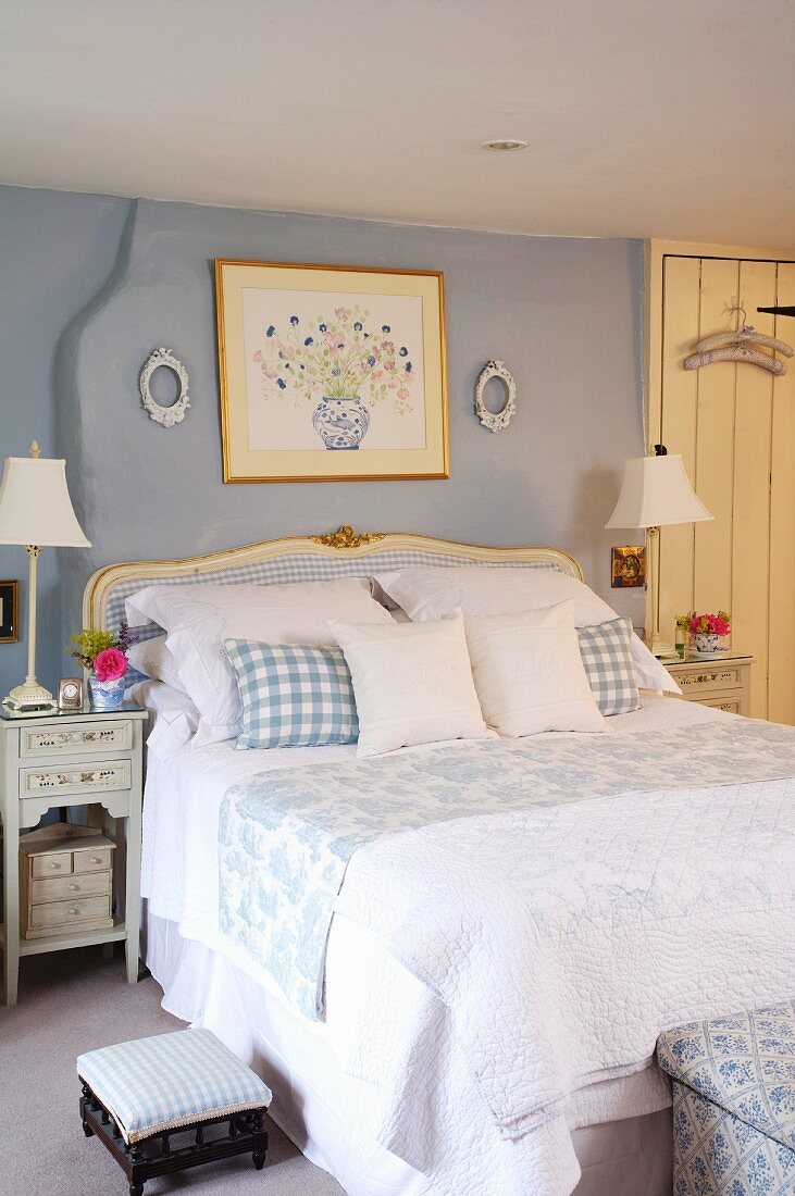 Schlafzimmer im antikisierenden Stilmix mit Doppelbett und hohen Lampen auf Nachtschränken; Deko mit pastellblau gemusterten Stoffen