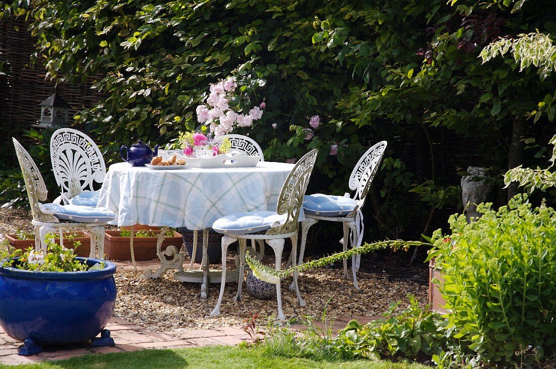 Runder Tisch und Gartenstühle aus weiss lackiertem Schmiedeeisen, gedeckt zur Teatime im Garten