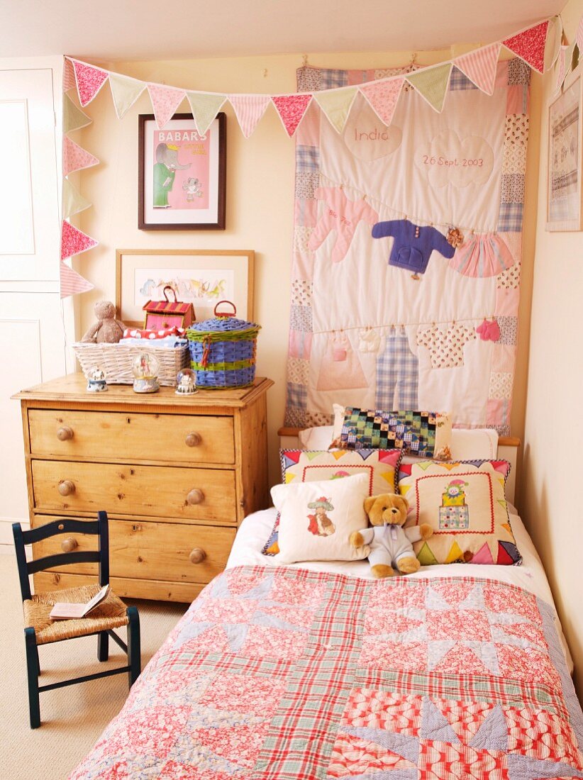 Rustikales Kinderzimmer - Bett mit Patchworkdecke neben schlichter Holzkommode und Wimpelgirlande vor Wandbehang