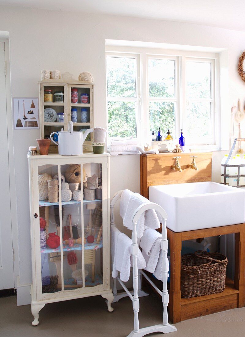 Trogartiges Waschbecken mit Holzunterbau am Fenster und Vintage Vitrinenschrank mit Badutensilien