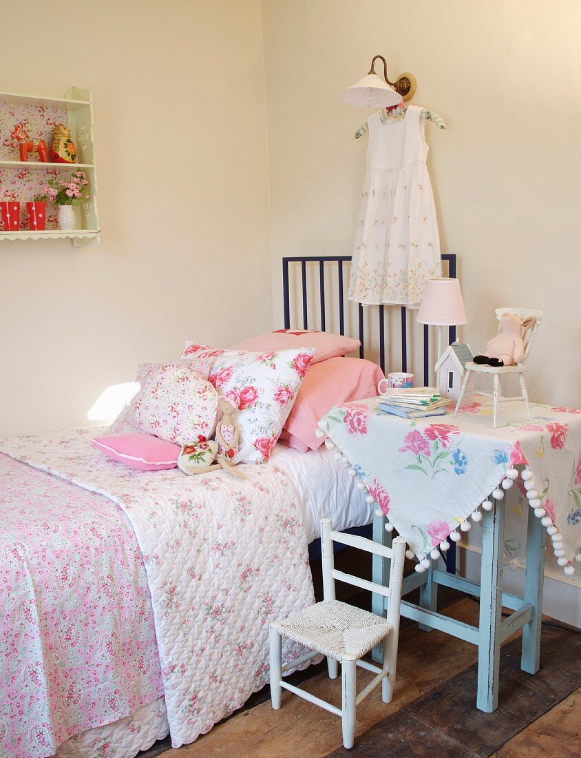Ländliche Kinderzimmerecke mit Blumenmotiven - Beistelltisch neben Kinderbett mit Blumenmuster auf Tagesdecke und Kissen