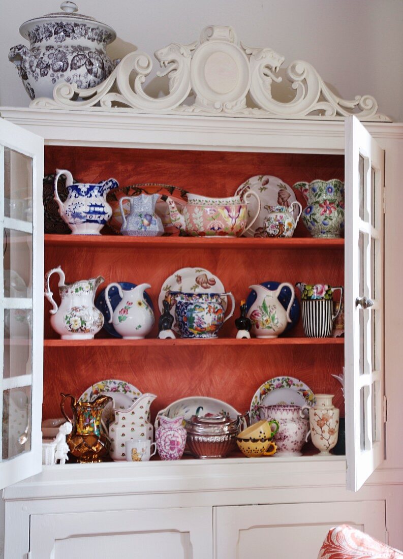 Weisser Küchenschrank mit Schnitzereien und Blick durch offene Türen auf antiquarische Porzellansammlung
