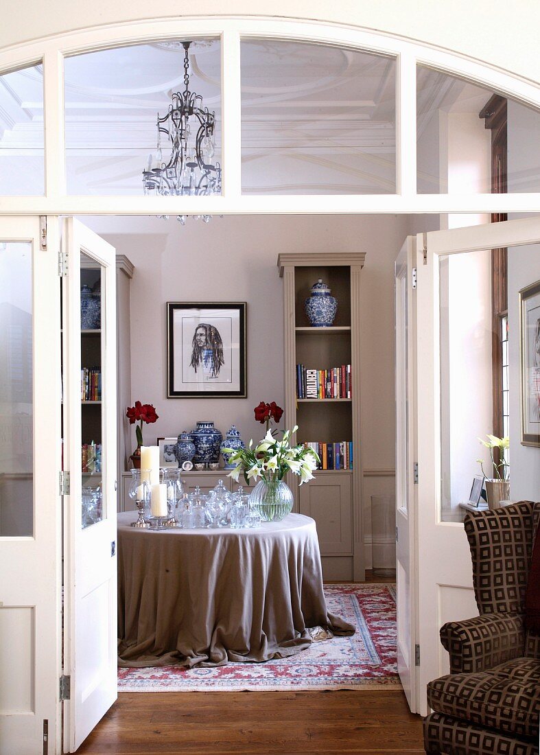 Blick durch offene Flügeltür auf Tisch mit bodenlanger Tischdecke im traditionellen Salon
