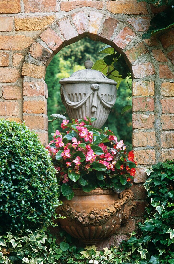 Fensterartige Öffnung in berankter Gartenmauer aus Ziegel mit Stein Urne