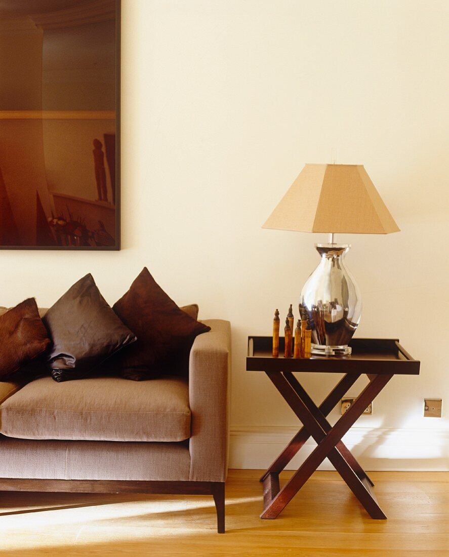 Wohnzimmer in Brauntönen mit Sofa, Tischleuchte auf Beistelltisch & Wandbild