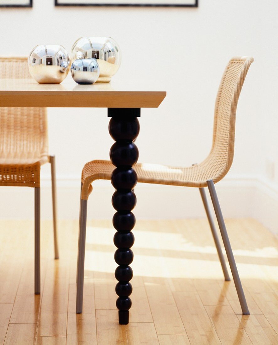 Korbstuhl an Esstisch aus Holz mit schwarzen, gedrechselten Tischbeinen (Ausschnitt)