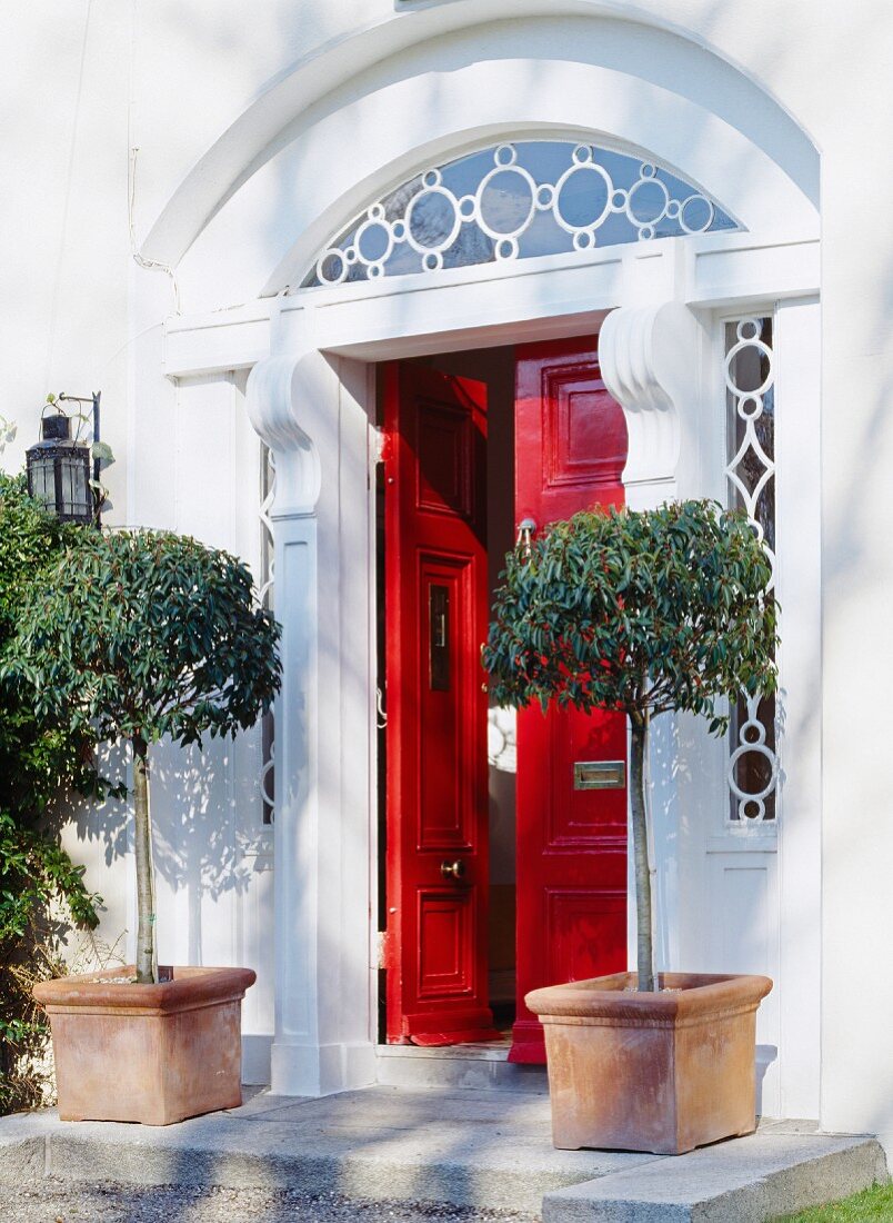 Hauseingang mit roter Flügeltür, verzierten Rundbogenfenstern & zwei Kübelpflanzen
