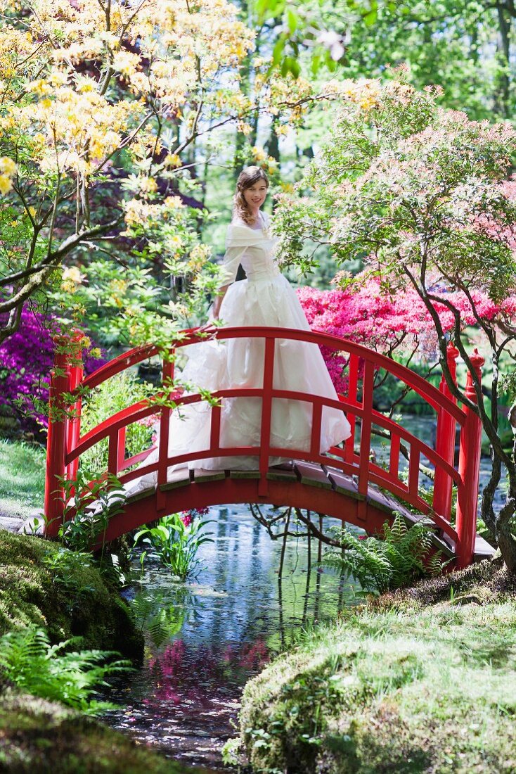 Bride in white wedding dress standing on red bridge in park