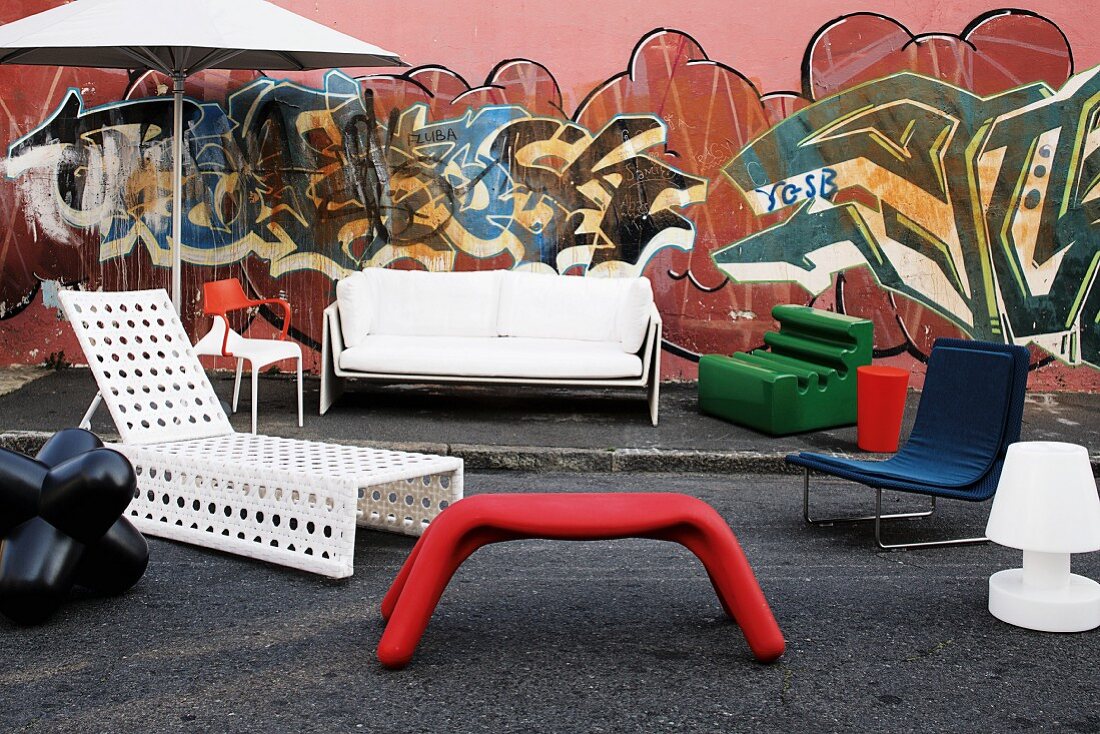 Trendige Sitzmöbel, Liege und Sonnenschirm für Garten und Terrasse vor einer mit Graffiti bemalten Hauswand