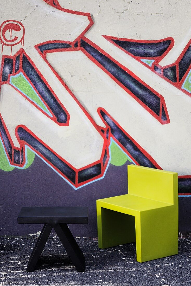 Schwarzes niederes Tischchen und grüner Stuhl vor einer mit Graffiti bemalten Hauswand