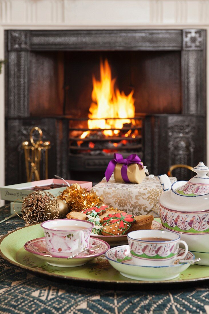 Traditionelles Porzellanservice und Weihnachtsplätzchen auf Tablett, im Hintergrund Kaminfeuer