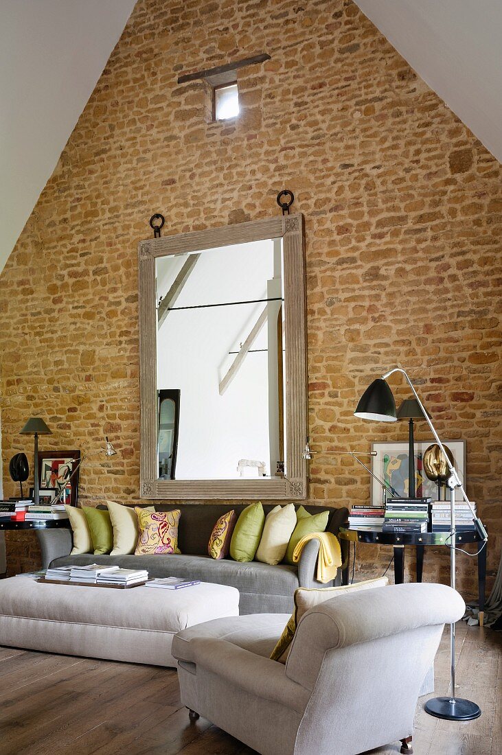 Übergroßer Wandspiegel an hoher Giebelwand einer umgebauten Scheune im Wohnbereich mit bequemen grau, weißen Polstermöbeln und Leseleuchte