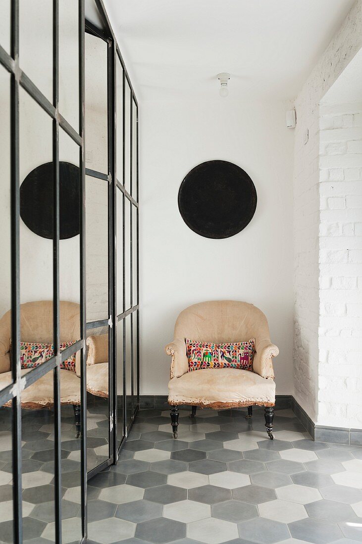Antique armchair on tiled floor in various shades of grey next to partition made from old mirrored panels