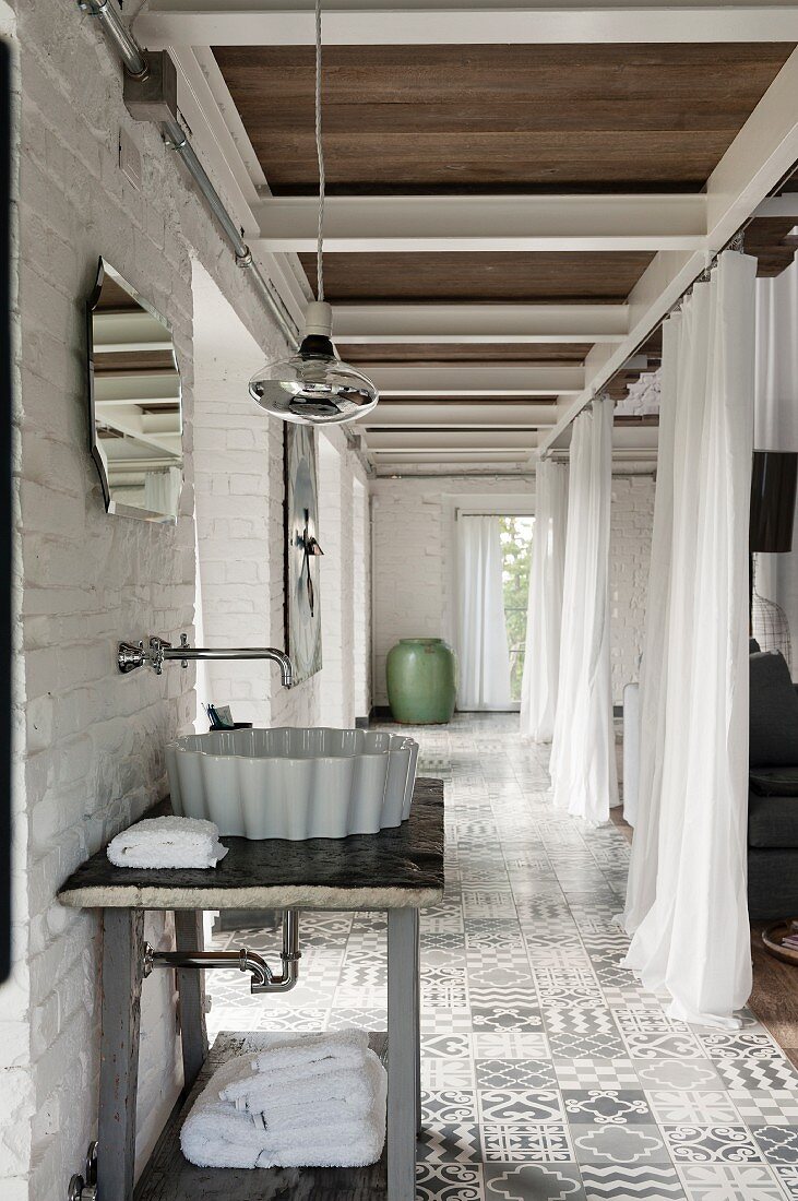 Waschschüssel auf schlichtem Tisch mit Wandarmatur in gefliestem Gangbereich, gegenüber offene Vorhängen als Raumteiler