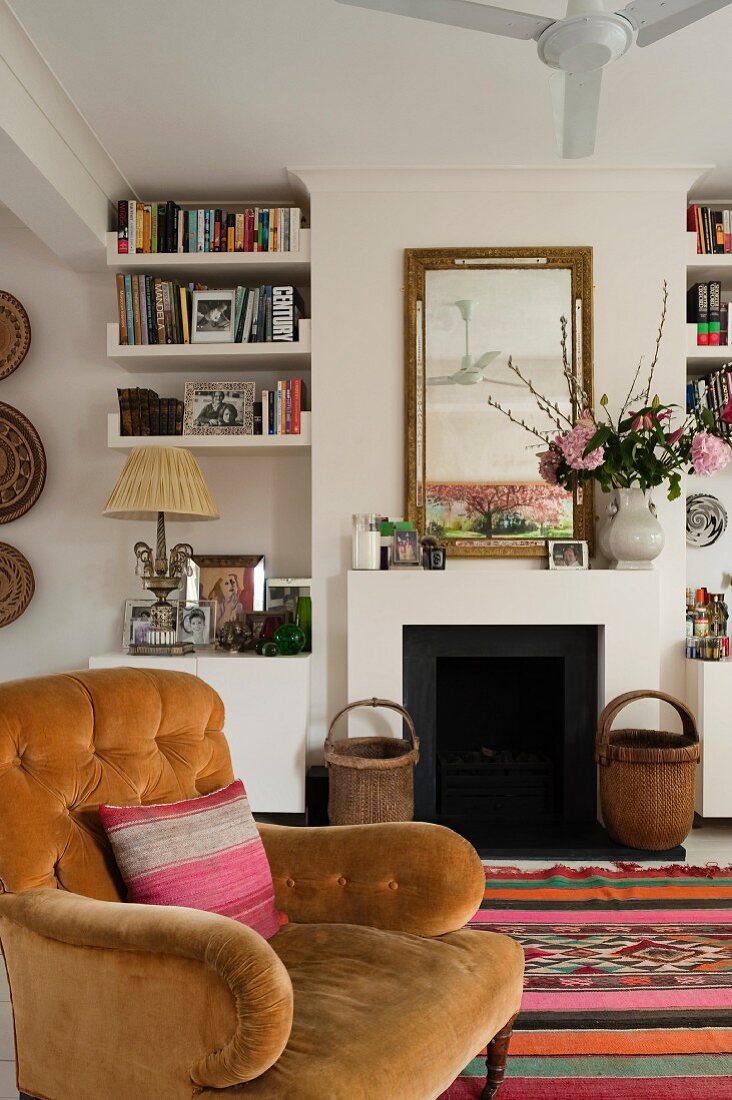 Living room with open fireplace, bookshelves and nostalgic velvet armchair on Moroccan rug