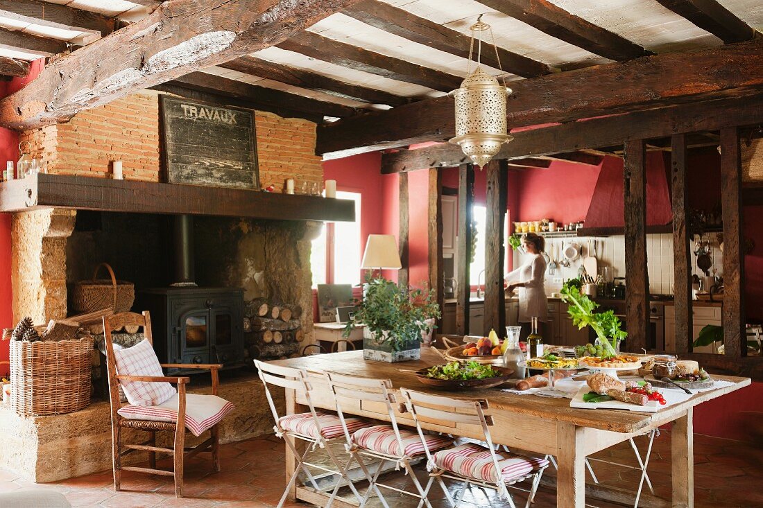 Grosse Wohnküche im französischen Landhaus mit alten Deckenbalken und Holzofen