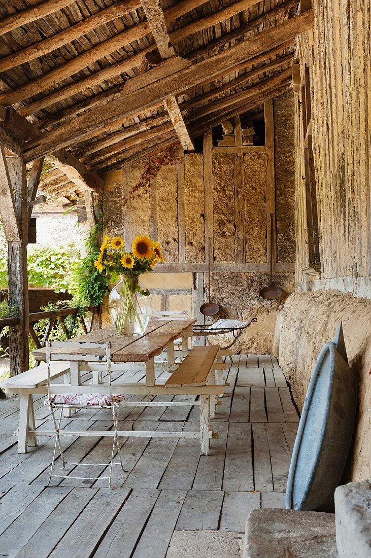 Sonnenblumenstrauss auf Tisch- Bankkombination auf rustikaler Veranda mit Holzdielen