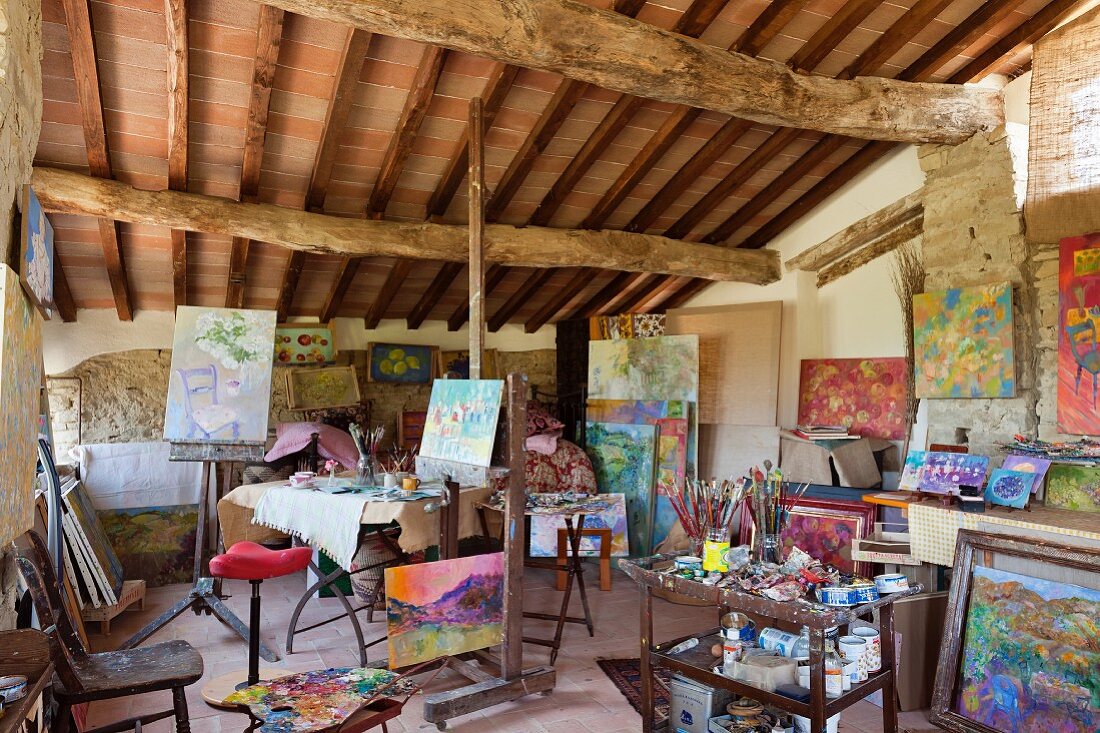 Colourful artworks in studio below rustic ceiling in Mediterranean holiday home
