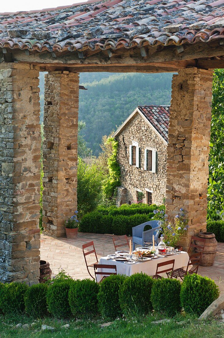 Blick auf festlich gedeckten Tisch, unter rustikalem Ziegeldach eines Terrassenplatzes in italienischer sommerlicher Landschaft