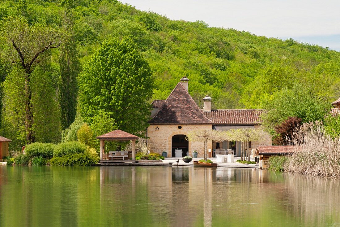 Blick über kleinen See auf eine französische Mühle aus dem 17. Jahrhundert; Hügellandschaft der Dordogne im Hintergrund