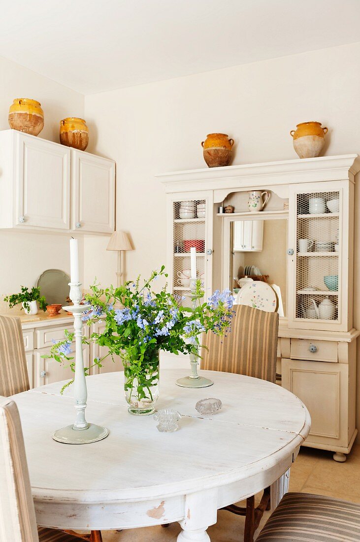 Dining room with country-house-style ceramic pots on dresser and candlesticks and flowers on oval dining table
